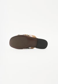 Sandale marron avec un dessus texturé, arborant un motif à rayures multicolores. Semelle plate avec une finition lisse et un bout légèrement arrondi.