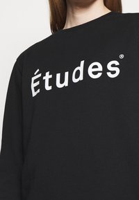 Sudadera negra de algodón, con un gran estampado blanco de "Études" en el pecho. Diseño de cuello redondo, mangas largas y textura sencilla.
