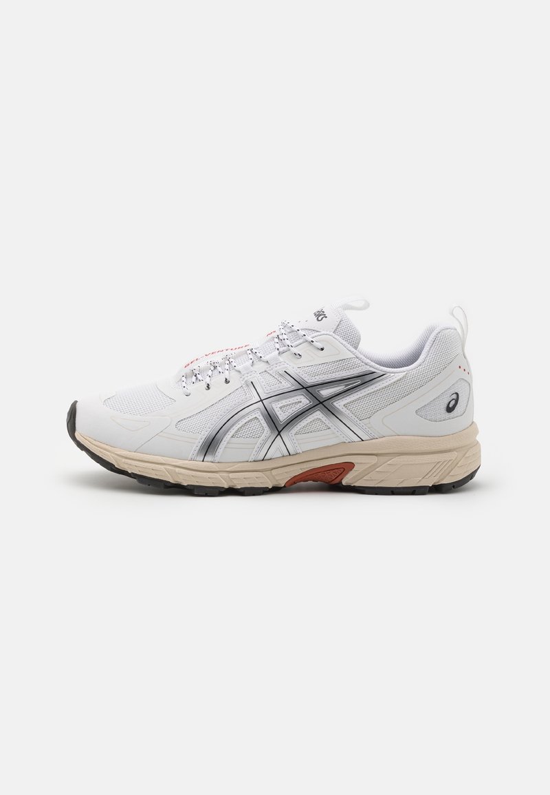 Chaussure de running blanche et beige avec logo latéral noir et gris, dessus en mesh et semelle en caoutchouc noire sur fond blanc.
