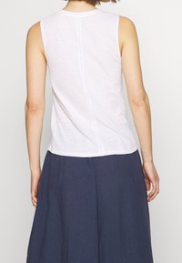 White sleeveless top made from lightweight fabric, featuring a subtle textured pattern and a straight back seam. Paired with a navy skirt.