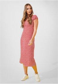 Czerwona kwiecista sukienka midi z krótkimi bufkami, dopasowanym gorsetem i falbaną u dołu. Noszona z białymi sneakersami na jednolitym tle.