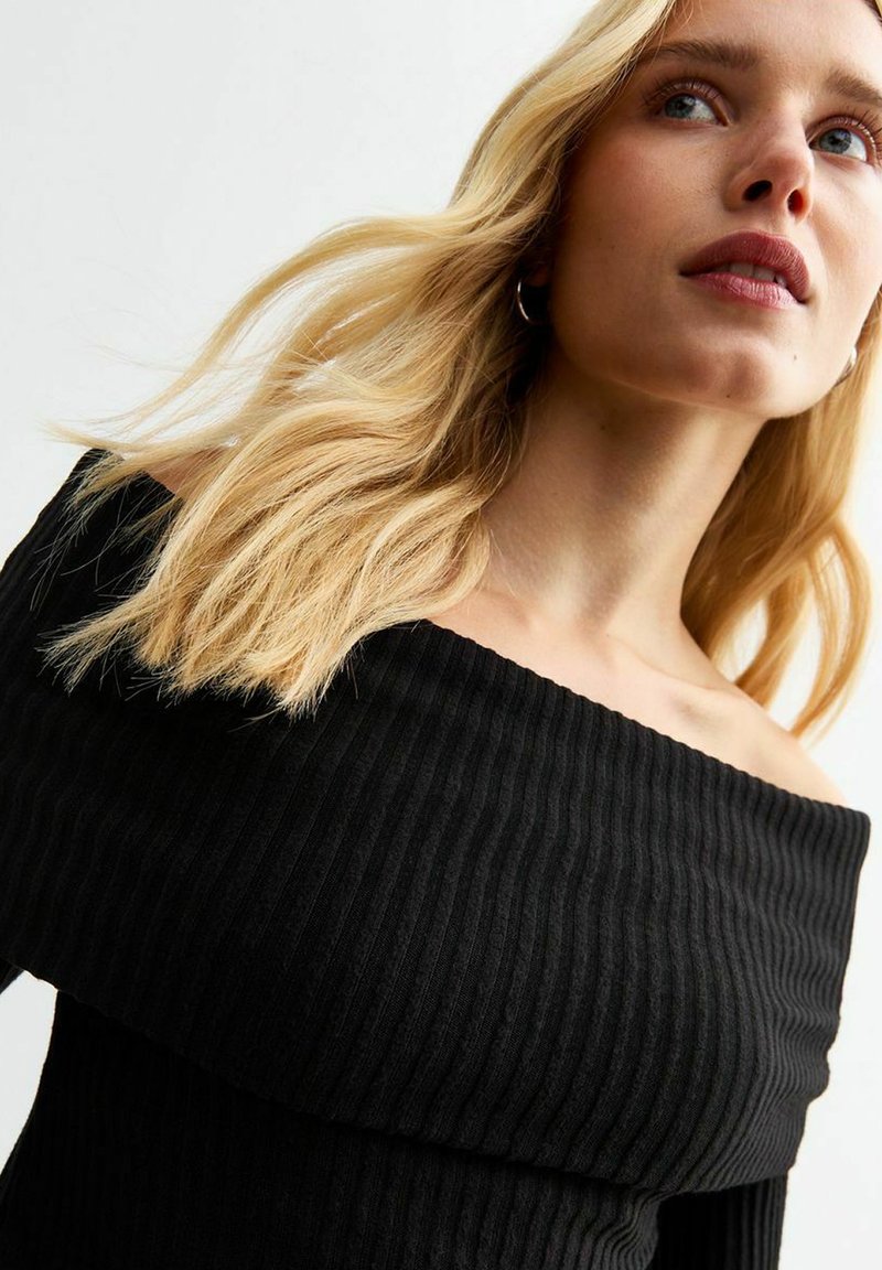 Abito nero senza spalle con texture a coste, design aderente e ampia scollatura, che mette in mostra un tessuto liscio e una silhouette definita.