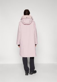 Cappotto da pioggia lungo e rosa con cappuccio, realizzato in materiale impermeabile e liscio. Presenta una vestibilità comoda e bottoni a pressione sul colletto.