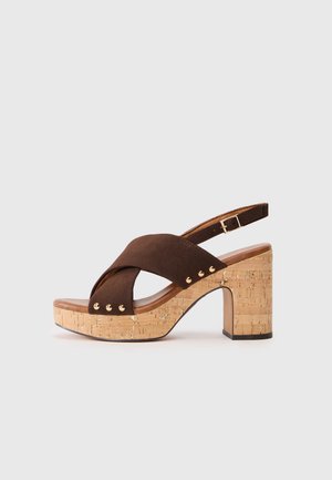 Brune ruskinds højhælet sandal med en korkblok hæl. Har tværstænger design, justerbar ankelrem og gyldne nitter på siden.
