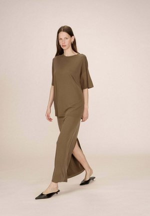 Femme marchant dans un haut court à manches courtes marron ample et un pantalon large assorti avec fente latérale, portant des escarpins à talons fins noirs.