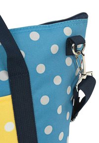 Bolsa de lunares azules con sección inferior amarilla, material de tela, herrajes plateados y una correa oscura. Cierre con cremallera en la parte superior.