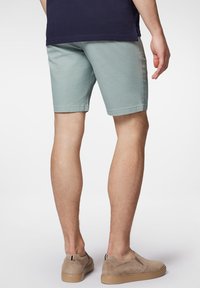 Jasnozielone bawełniane szorty o prostym kroju z kieszeniami bocznymi, w zestawieniu z beżowymi butami wsuwanymi o teksturowanej powierzchni i czarnymi akcentami.