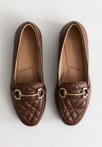 Braune synthetische Slipper mit gestepptem Muster, ausgestattet mit goldenen Metalldetails und einem glatten Futter. Klassisches Schlupfdesign.