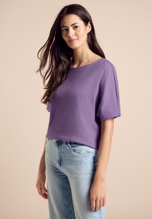 Top violet à manches courtes côtelé avec un col large, associé à un jean en denim bleu clair. Texture lisse et coupe décontractée.