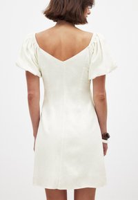 Weißes Leinenkleid mit Puffärmeln und einem V-förmigen Rücken. Einfaches Design mit tailliertem Oberteil und ausgestelltem Rock. Minimalistische Details.