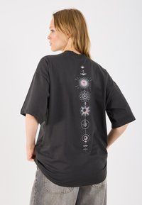 T-shirt preta de algodão com mangas curtas, apresentando estampas celestiais em branco e rosa ao longo do centro das costas. Design solto.