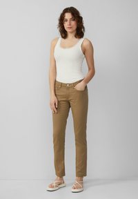 Dopasowany, jasnobeżowy top na ramiączkach z koronkowym wykończeniem, w połączeniu z wąskimi, khaki spodniami z bocznymi kieszeniami i pojedynczym zapięciem na srebrny guzik.