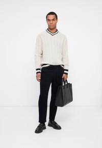 Licht beige kabel gebreide trui met V-hals en zwarte accenten. Donker marineblauwe broek, zwarte lederen schoenen en een gestructureerde zwarte tote tas.