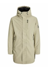 Beige vandtæt jakke med hætte, lynlåslukning foran og sidelommer. Har sort indvendig foring og logo-detalje på ærmet.