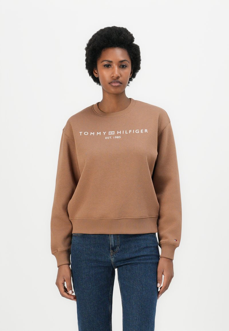 Hnědá mikina vyrobená z bavlněné směsi s žebrovanými manžetami a lemem. Na hrudi je bílé logo s textem "TOMMY HILFIGER" a "EST. 1985".