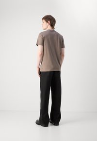 Ruda trumpa rankovė t-shirt pagaminta iš medvilnės, derinama su juodomis plačiomis kelnėmis ir juodais batais, matoma iš užpakalio. Paprastas dizainas, minimalūs detalės.
