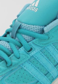 Turkos atletisk sneaker med en ovandel i mesh och mocka, med ton-i-ton snören och Adidas-logotypen på tungan. Texturerad gummisula.