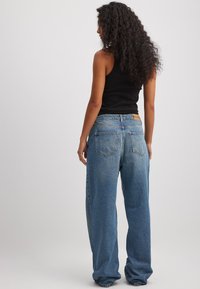 Šviesiai mėlyni džinsai su platesnėmis kojomis, vidutinio plovimo, su galiniais kišenėmis ir rudos spalvos etikete ant juosmens.