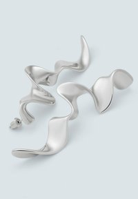 Silberner metallischer Ohrcuff mit einem wellenförmigen, skulpturalen Design. Die glatte Oberfläche und die variierende Dicke sorgen für visuelles Interesse. Sicherer Verschluss ist enthalten.