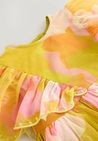 Close-up of colorful fabric with yellow, orange, pink, and green patterns and ruffled sheer mesh detailing on a garment.