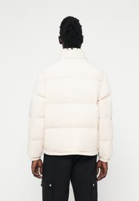 Pūdera jaka off-white krāsā ar pāršūtu tekstūru, augstu apkakli un elastīgām piedurknēm, ar taisnu apakšmali un brīvu piegriezumu.