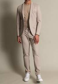 Beige sako přes odpovídající fitted tričko a kalhoty na stahovací šňůrku. Bílé tenisky dotvářejí outfit a obsahují detaily kapesníčku.