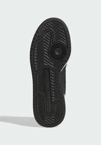 Musta lenkkarin pohja, jossa on teksturoitu kumipinta, sisältäen aaltoilevan kuvion ja pyöreän pidon elementin keskellä. Brändin logo painettuna.