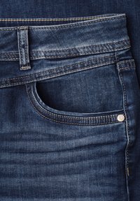 Primer plano del bolsillo de unos vaqueros de mezclilla azul con presilla de cinturón visible, costura en la costura y detalle de remache metálico.