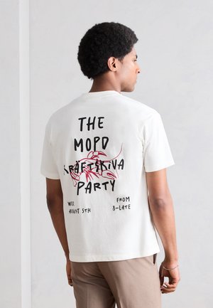 Άνδρας με κοντά σγουρά μαλλιά που φοράει λευκό μπλουζάκι με κόκκινο κάβουρα ποταμού και μαύρο κείμενο που προωθεί πάρτι με ποδήλατο και κάβουρα στον πίσω μέρος.