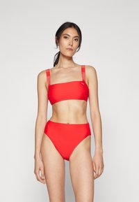 Červený bikiny s bandeau vrchnou časťou a vysokými pásmi. Obsahuje popruhy s logom a hladký, elastický materiál. Jednoduchý, jednofarebný dizajn.