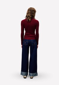 Bordeaux geribbelde coltrui gecombineerd met donkerblauwe wijde jeans met omslagen en twee achterzakken met stikselaccenten.