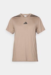 T-shirt de sport tan fabriqué dans un tissu lisse, avec des accents noirs sur les épaules et un logo Adidas noir centré sur la poitrine.