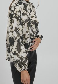 Blusa in tessuto leggero e trasparente con un motivo astratto in bianco e nero. Collo alto con maniche a sbuffo arricciate e polsini elastici.