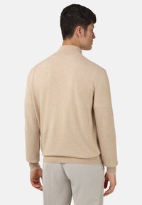 Pull en maille beige avec un col arrière et des manches longues. Texture douce, poignets et ourlet côtelés, design uni, adapté à une tenue décontractée.