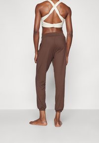 Brązowe, zwężane spodnie dresowe z elastycznymi mankietami i bocznymi kieszeniami, zestawione z jasnobeżowym sportowym biustonoszem z krzyżującym się tyłem.