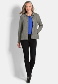 Kraagjack in zwart-wit geblokt patroon, gecombineerd met een helderblauw topje en zwarte broek. De stof lijkt soepel met een getailleerde pasvorm.