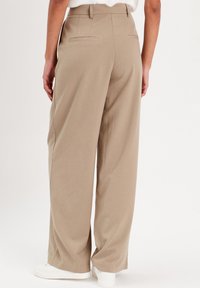 Pantaloni a gamba larga beige in un tessuto liscio con vita tailored e due tasche posteriori. Abbinati a sneakers bianche.
