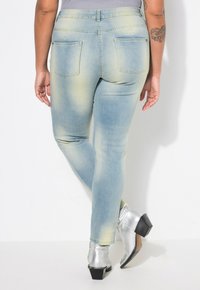 Jean en denim bleu clair avec un effet délavé, comportant deux poches arrière, une taille mi-haute et une coupe slim. Porté avec des bottines argentées métalliques.