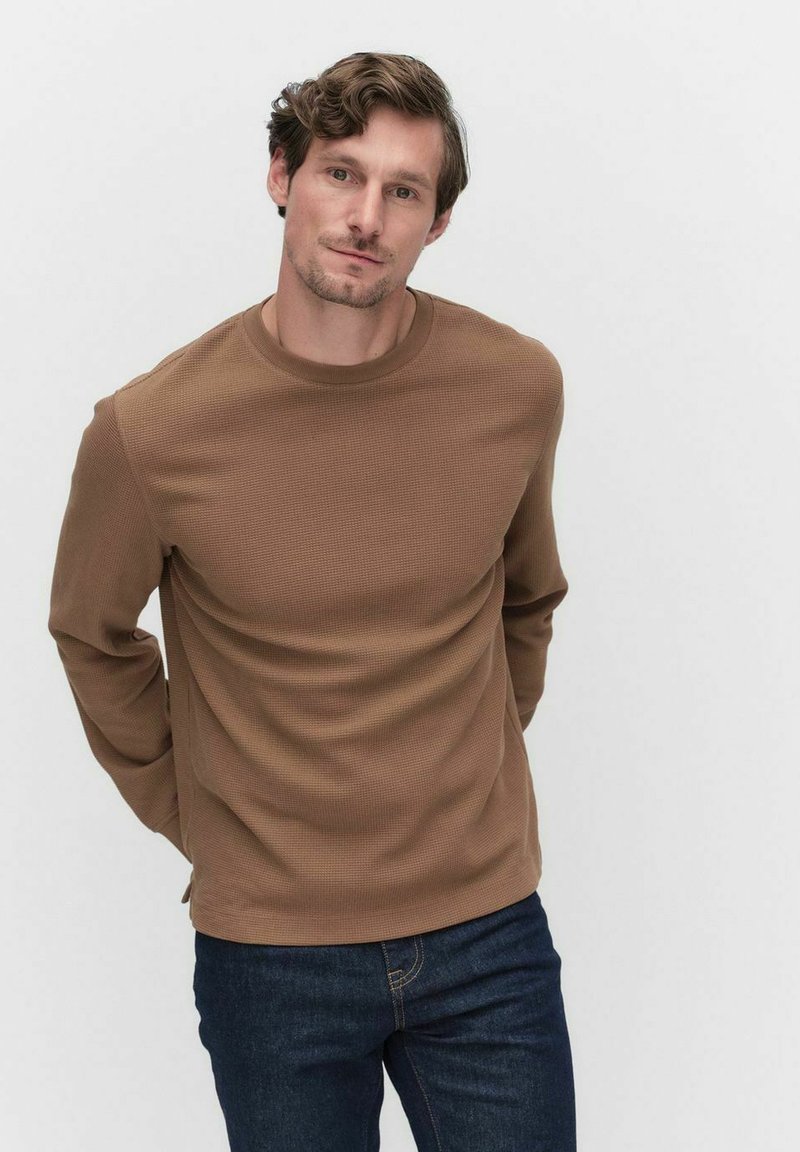 Brun ribbad långärmad tröja med rund halsringning, i kombination med mörkblå jeans. Tyget har ett strukturerat mönster.