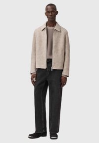 Beige uldblandingsjakke med krave, lynlås lukning, sidelommer, parret med grå ribbede sweater og mørke denim bukser, sorte støvler.