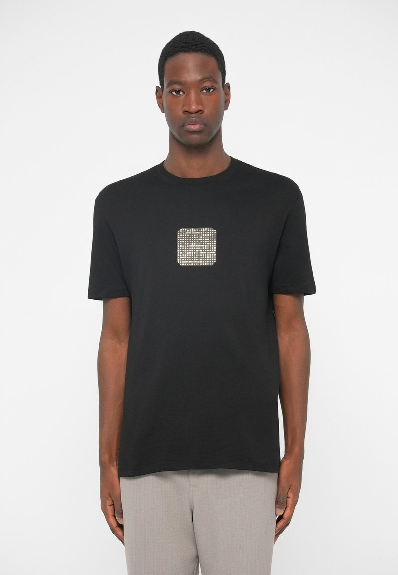 Camiseta preta com um design texturizado em forma de quadrado de cor metálica ao centro. Tem mangas curtas e um decote redondo.