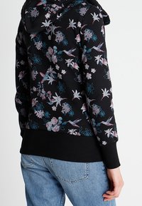 Zwarte hoodie met kleurrijke bloemen- en vogelprint. Zachte stof, ribbelboorden en -zoom, verstelbare capuchon. Casual pullover ontwerp.