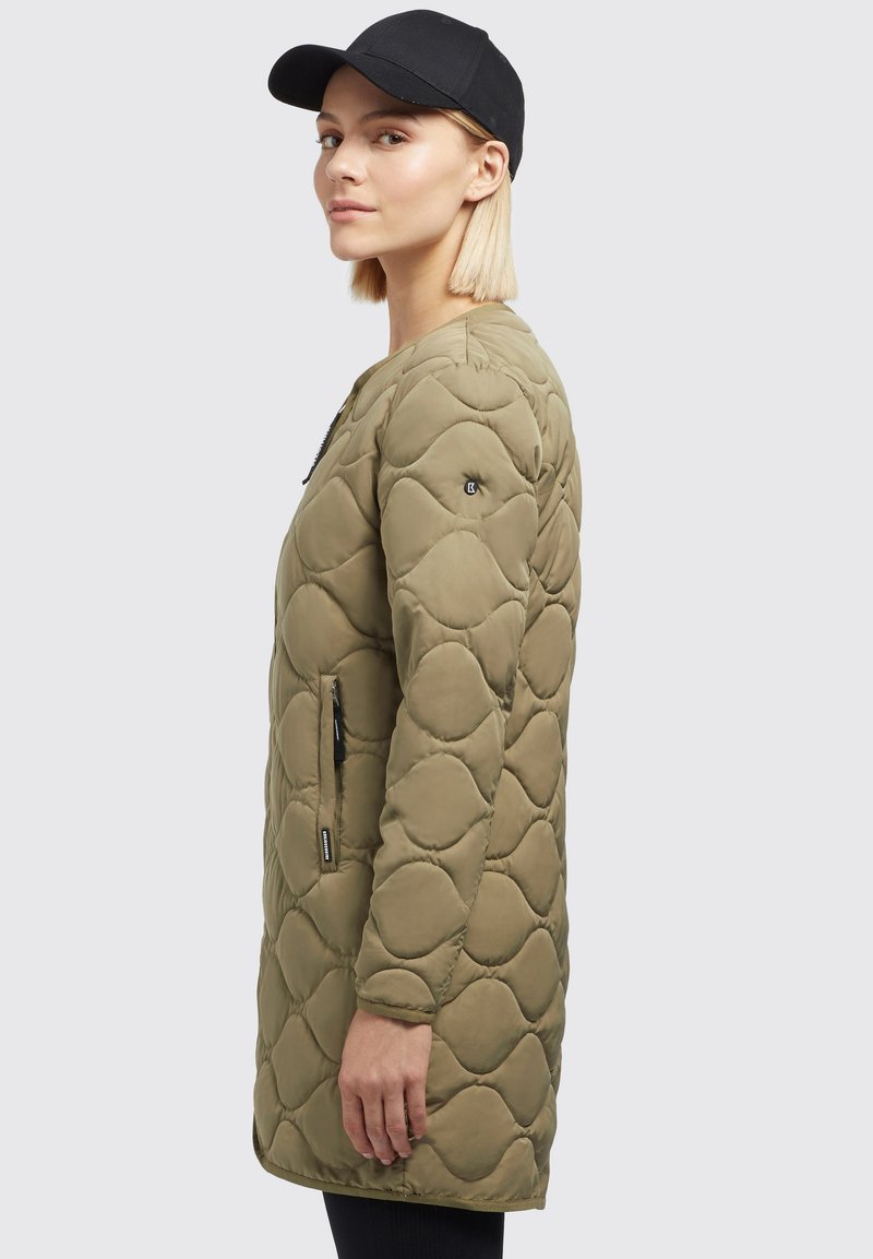 Quilted olivgrüner Mantel mit mittellangem Design, seitlichen Reißverschlusstaschen, rundem Halsausschnitt und einer eleganten, glatten Textur. Schwarze Mütze getragen.