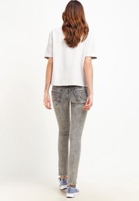 Haut gris clair à manches courtes associé à un jean skinny gris délavé et des chaussures de sport bleues, avec des poches arrière et une coupe décontractée.