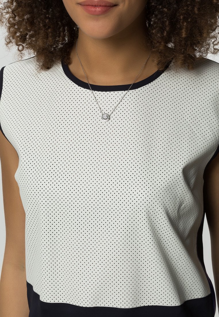Top bianco e blu marino con maniche corte, caratterizzato da un motivo a pois e una texture liscia. Scollatura rifinita in blu marino. Design semplice.