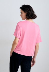 Light pink short-sleeve T-shirt in a relaxed fit, featuring a round neckline and soft fabric, paired with dark patterned trousers.