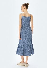 Blauwe bloemen midi-jurk met dunne banden, met een gelaagde ruches onderkant, gemaakt van lichtgewicht stof. Draag met beige instap schoenen.
