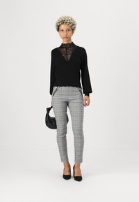 Black sweater with lace detail at the neckline, gray plaid trousers with zippered pockets, and black high heels, holding a black handbag.