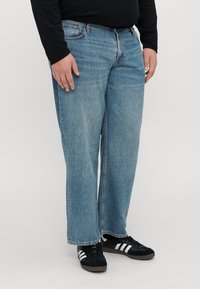 Jeans in denim azzurro chiaro con vestibilità loose, dotati di cinque tasche e chiusura a zip, abbinati a sneakers nere con strisce bianche.