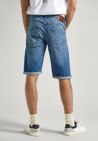 Shorts de denim en azul claro con dobladillos enrollados, que presentan una etiqueta trasera de cuero marrón y dos bolsillos traseros con costuras en contraste.